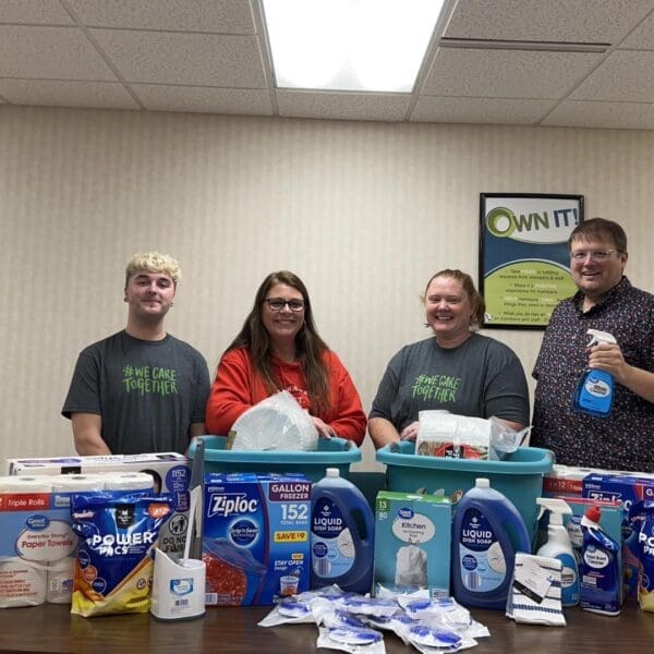 Group of four volunteers standing behind table full of cleaning products.