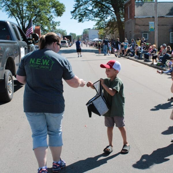 Credit union staff member passing out candy to young children during parade.