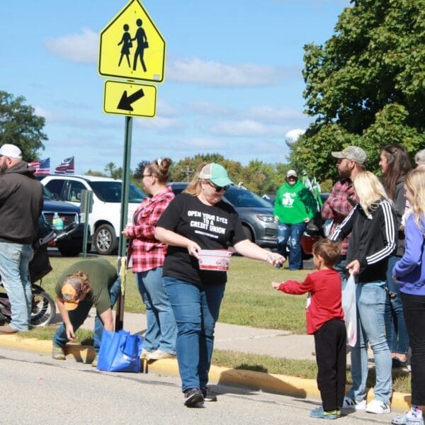 Volunteer passing out candy to people standing along sidewide for event.