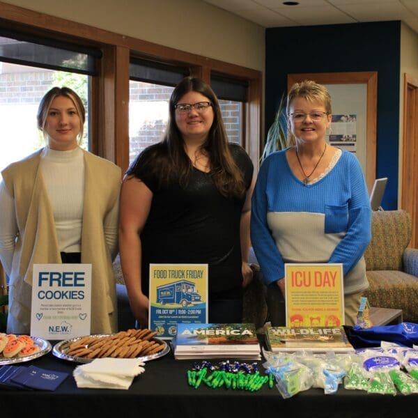 Group of three women standing behind display table with signs for Free Cookies, Food Truck Friday and ICU Day.