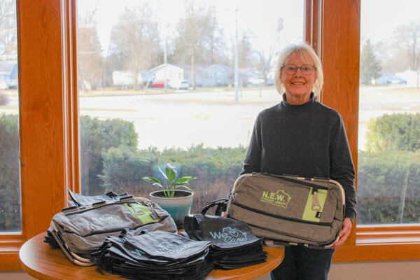 Woman standing next to large windows holding a branded N.E.W. credit union bag.