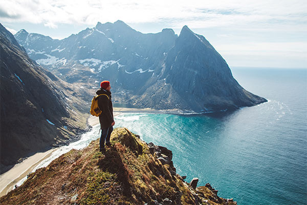 Man standing on the edge of mountain side looking out at large body of water.