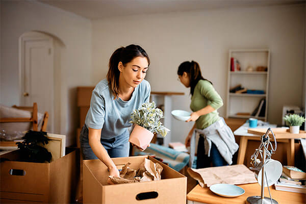 Two women placing belongings in moving boxes.