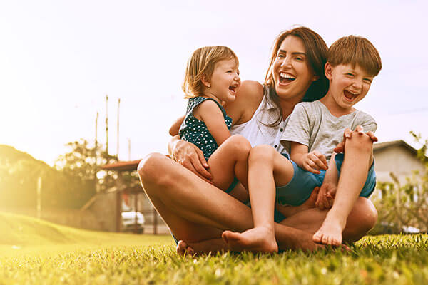 Mother holding children in her lap outside on grass.