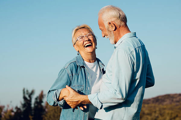 Old retired couple smiling and holding onto one another.