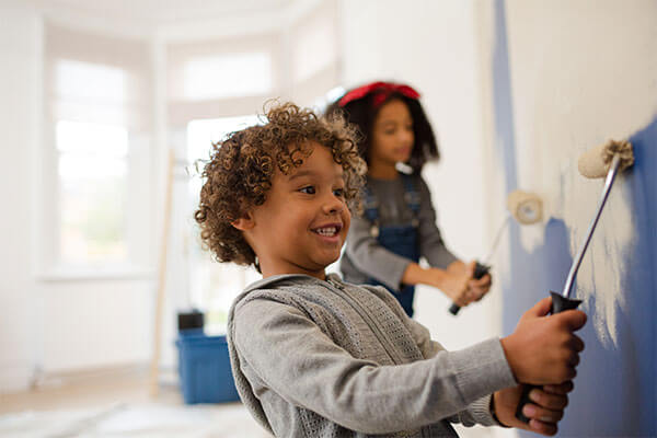 Two young children painting with rollers on wall in blue paint.