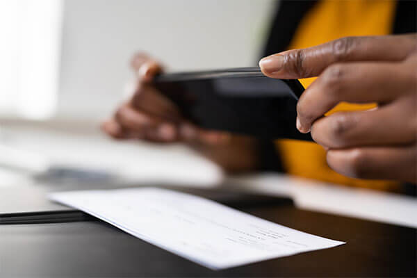 Person holding phone horizontally taking photo of check on desk.