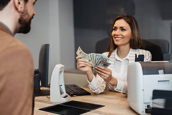Woman holding American dollar bills in her hands while talking to customer on other side of desk.