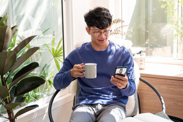 Handsome Asian teenager man wearing casual clothes in glasses using smart phone browsing Internet on mobile phone device at the living room.